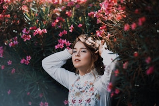 woman wearing white floral long-sleeved top standing beside pink flowers