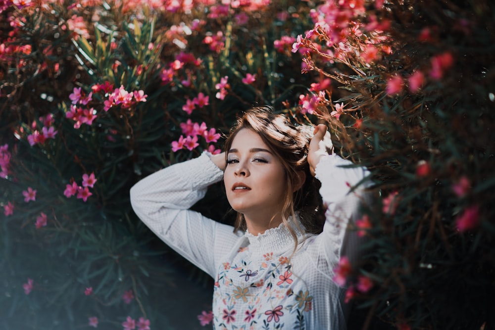 woman wearing white floral long-sleeved top standing beside pink flowers