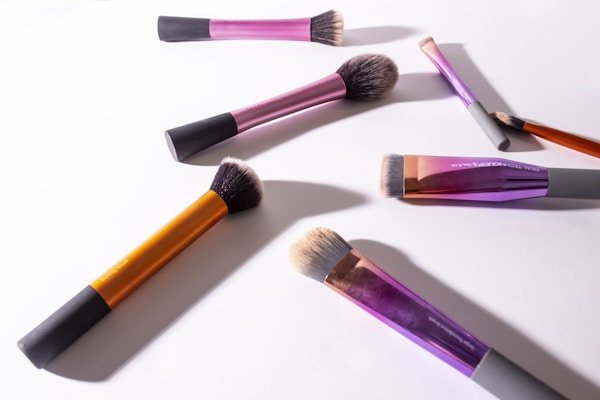 An assortment of makeup brushes with wooden handles resting beside a mirror reflecting warm light.