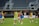 A group of female soccer players are on a field, wearing training bibs over their uniforms. They are practicing with a soccer ball, engaged in a passing drill. The stadium appears empty except for a few spectators and staff. The players are focused and in motion, showing dynamic movement.