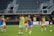 A group of female soccer players are on a field, wearing training bibs over their uniforms. They are practicing with a soccer ball, engaged in a passing drill. The stadium appears empty except for a few spectators and staff. The players are focused and in motion, showing dynamic movement.
