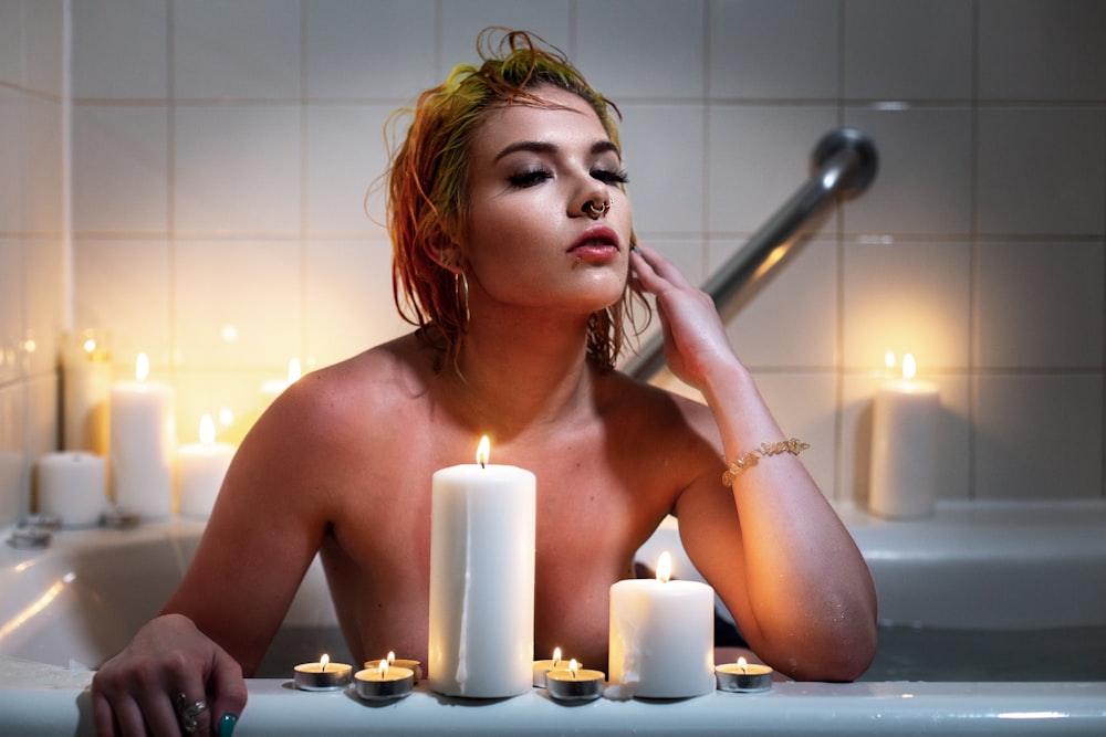 Frau sitzt in der Badewanne hinter brennendem Teelicht und Stumpenkerzen