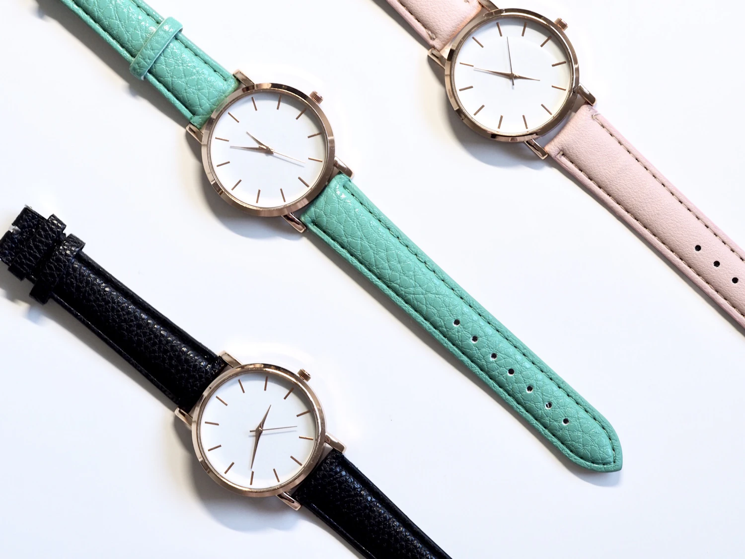 Three white-dial watches on mint, pink and black calf straps laid out on white