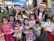 Parents and children exploring a colorful local market, smiling and holding hands.