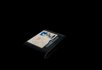 A vintage video game cartridge with a prominent blue character on the label is set against a completely black background. The design includes dynamic illustrations, likely related to the game's theme, with playful sketches in red and a color palette that draws the eye to the cart's detailed artwork.