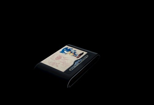 A vintage video game cartridge with a prominent blue character on the label is set against a completely black background. The design includes dynamic illustrations, likely related to the game's theme, with playful sketches in red and a color palette that draws the eye to the cart's detailed artwork.