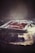 A metal tray filled with seasoned meat pieces is positioned on a charcoal grill emitting gentle smoke. The atmosphere is dimly lit, creating a rustic and warm ambiance.