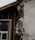 A section of a building with exposed and damaged wall layers is visible. The surface shows crumbling plaster revealing the brick and insulation beneath. A window with a white frame is partially seen, surrounded by unfinished wooden beams.