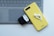 A yellow phone case with wireless earbuds sits on top of a laptop keyboard. An open black charging case for the earbuds is nearby.