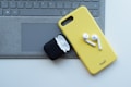 A yellow phone case with wireless earbuds sits on top of a laptop keyboard. An open black charging case for the earbuds is nearby.