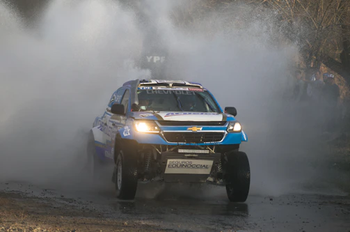 Side view of the rally car crossing a shallow river with water splashing around.
