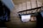 A staircase with wooden steps and a metal railing is shown from a top-down perspective. At the base of the stairs, there is a small table with a decorative doily and a floral arrangement. A pile of white linens or pillows rests beside the table, adding a homely touch.