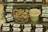 A variety of packaged cheese blocks labeled 'Face Rock Pepper Alpine' are displayed on a metal surface. In the center, a clear container holds cubed cheese pieces with visible herbs. Beside it, a green container filled with wooden toothpicks. Containers of a spreadable substance are on the left.