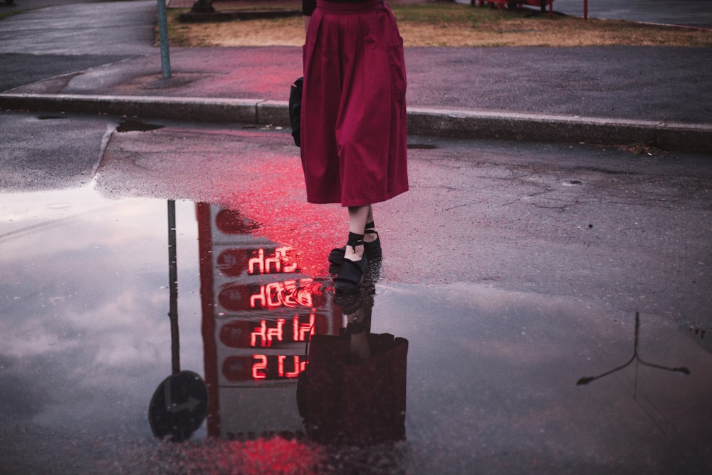 woman standing on road beside water reflecting gasoline station's price signage