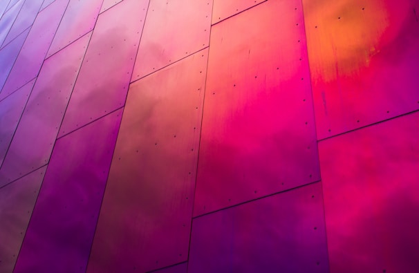 Large metal panels display vibrant shades of pink, purple, and orange. The surface is smooth yet slightly textured, with visible rivets at regular intervals.