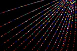 Colorful triangular flags are strung across a dark background in parallel lines, creating a vibrant and festive atmosphere. The flags are arranged in various colors such as red, blue, green, yellow, and pink.