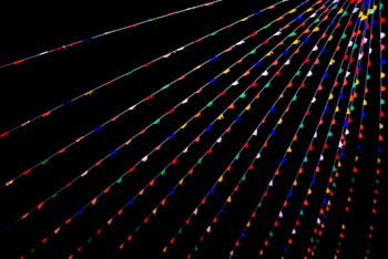 Colorful triangular flags are strung across a dark background in parallel lines, creating a vibrant and festive atmosphere. The flags are arranged in various colors such as red, blue, green, yellow, and pink.