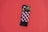 A pair of colorful patterned socks with a geometric cube design featuring red, black, and white colors is placed on a solid red background. The socks are neatly folded, and there is a cardboard label attached near the top bearing the brand name.