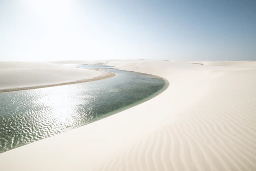 A stunning aerial view of Lençóis Maranhenses with its crystal-clear lagoons and white sand dunes under a bright blue sky.