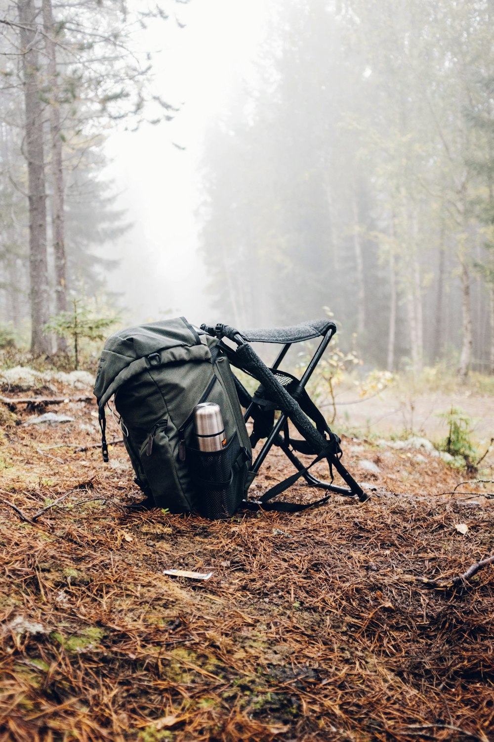 black and gray backpack with camping chair on forest