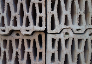 Four stacked hollow concrete blocks with a light beige color, displaying rough surfaces and multiple rectangular openings.