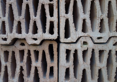 Four stacked hollow concrete blocks with a light beige color, displaying rough surfaces and multiple rectangular openings.