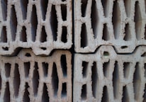 Four stacked hollow concrete blocks with a light beige color, displaying rough surfaces and multiple rectangular openings.