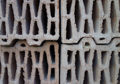 Four stacked hollow concrete blocks with a light beige color, displaying rough surfaces and multiple rectangular openings.