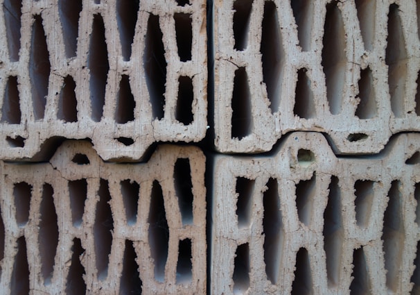 Four stacked hollow concrete blocks with a light beige color, displaying rough surfaces and multiple rectangular openings.