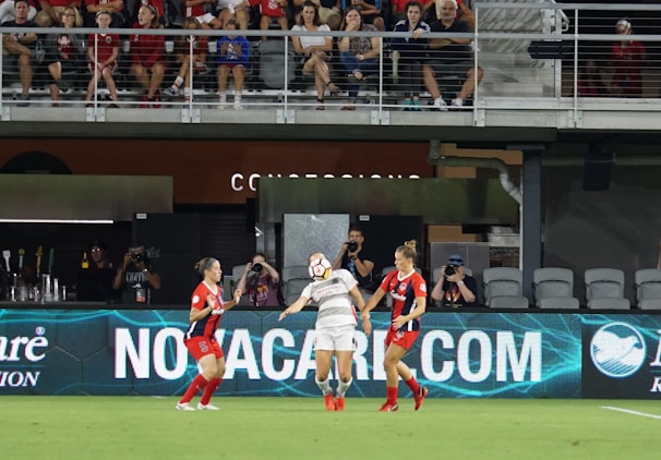 Crowd cheering enthusiastically as female players pass the ball on a lively football field.