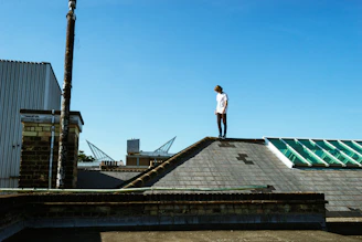 A skilled roofer inspecting a residential roof under a clear blue sky in Valley Stream.
