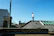 Professional roofer inspecting shingles on a residential roof under clear blue skies.
