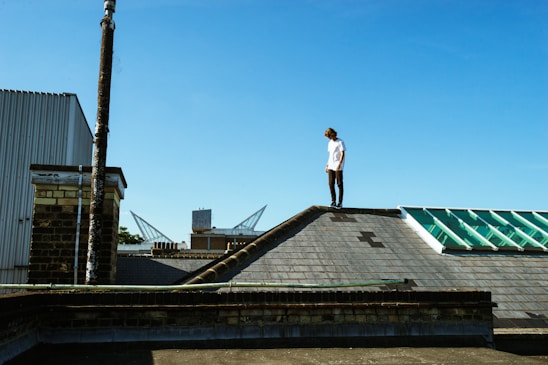 A professional roofer inspecting a residential roof under clear skies