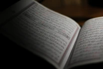 Close-up of an open Quran with traditional Islamic calligraphy illuminated by soft natural light.
