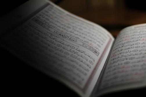 A close-up of an open Quran with elegant Arabic calligraphy under soft blue lighting.