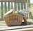 A wicker picnic basket with the letters 'F & M' is resting on a wooden bench. The basket contains bundles of fresh lavender flowers.