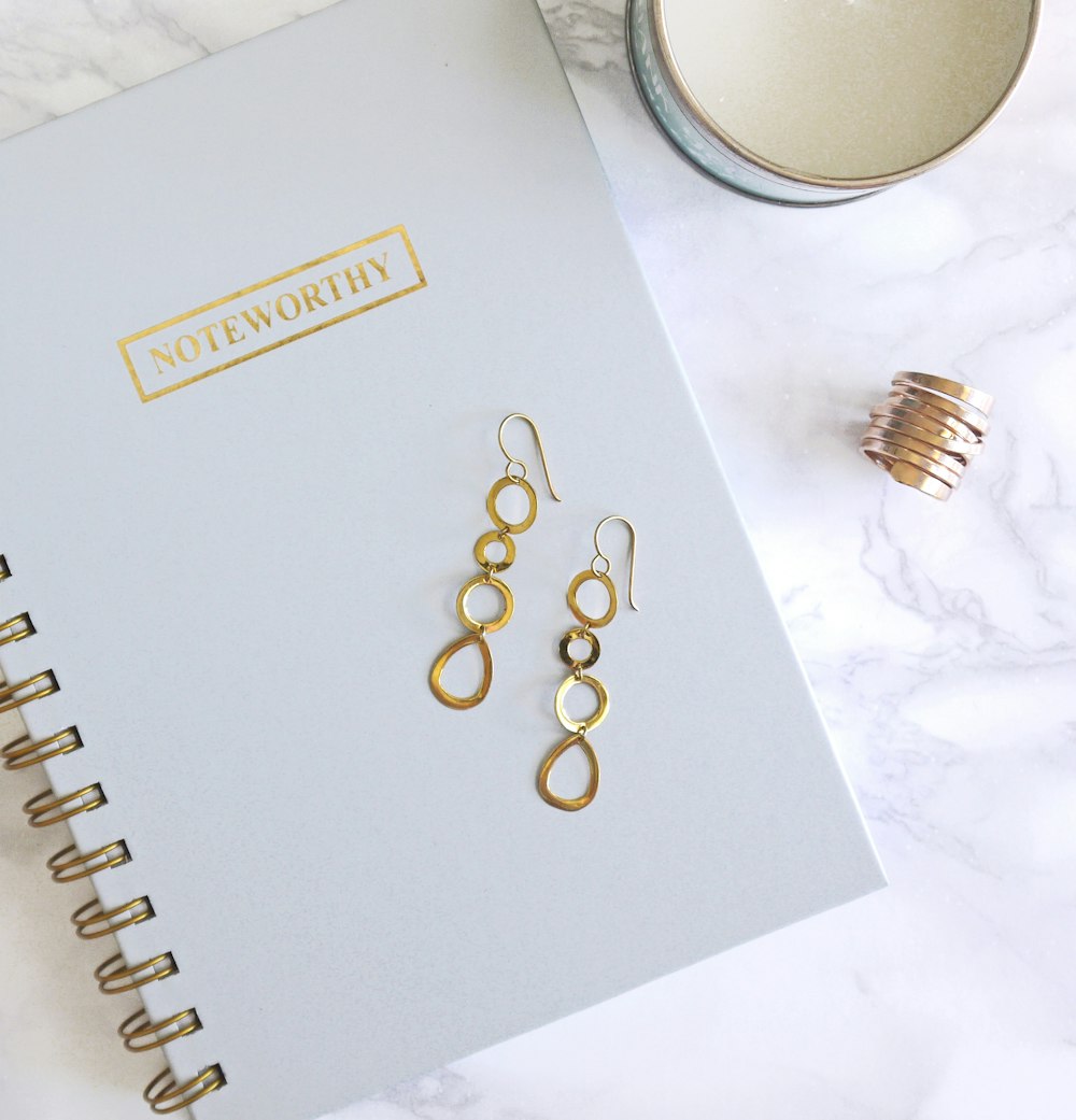 pair of gold-colored dangling hook earrings on top of spiral notebook