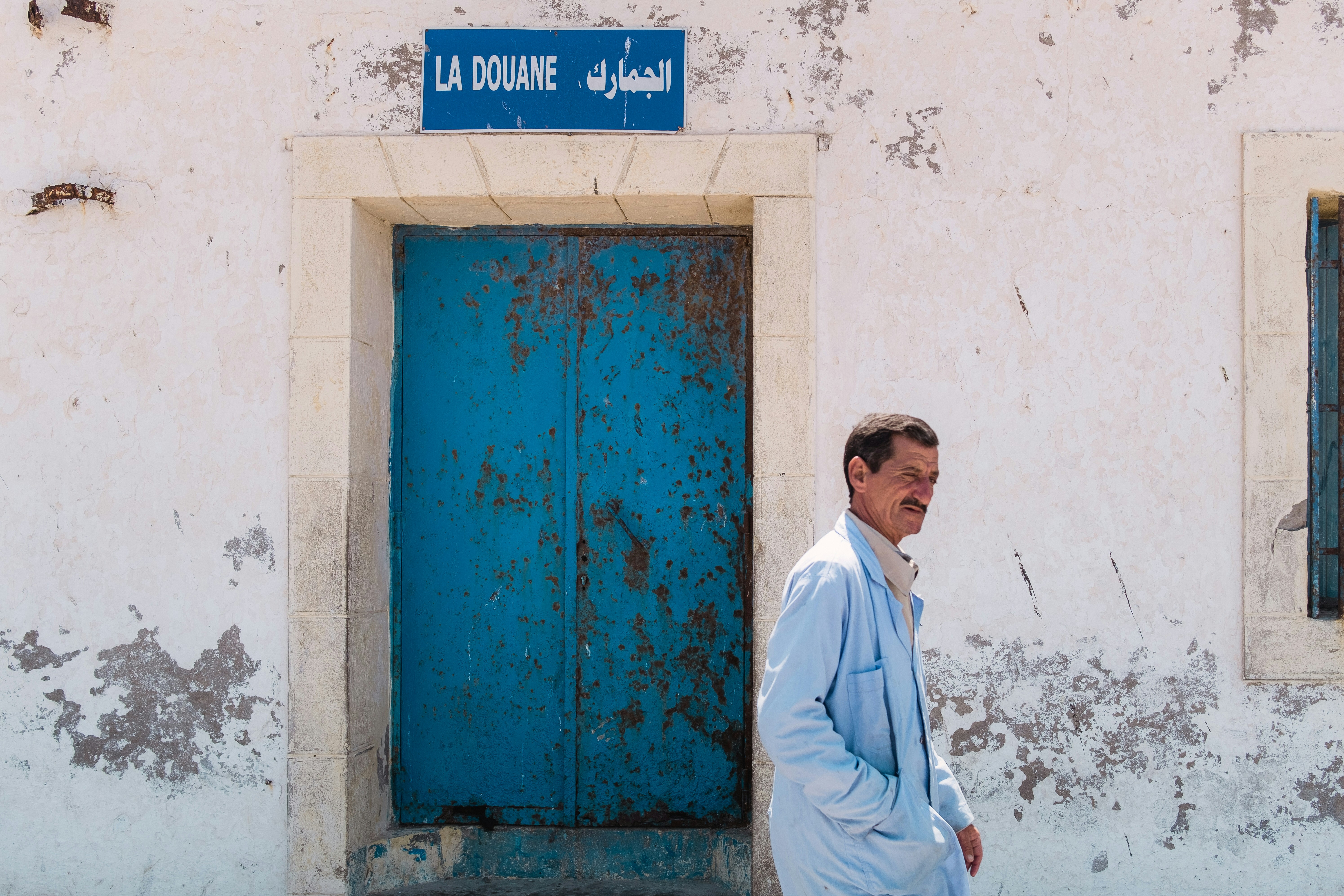 A man snickers in front of a rusted blue door near the citadel in Essaouira.