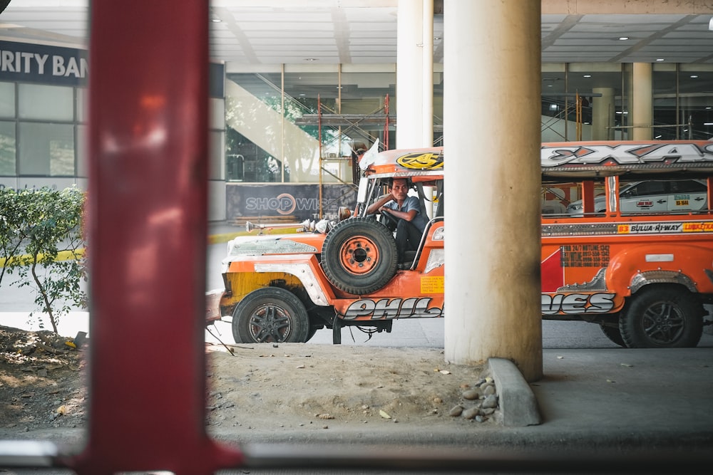 an orange jeep driving down a street next to a tall building