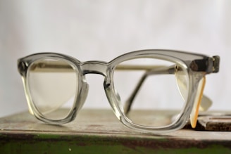 A pair of vintage eyeglasses with a clear, chunky frame resting on a surface with a blurred background.