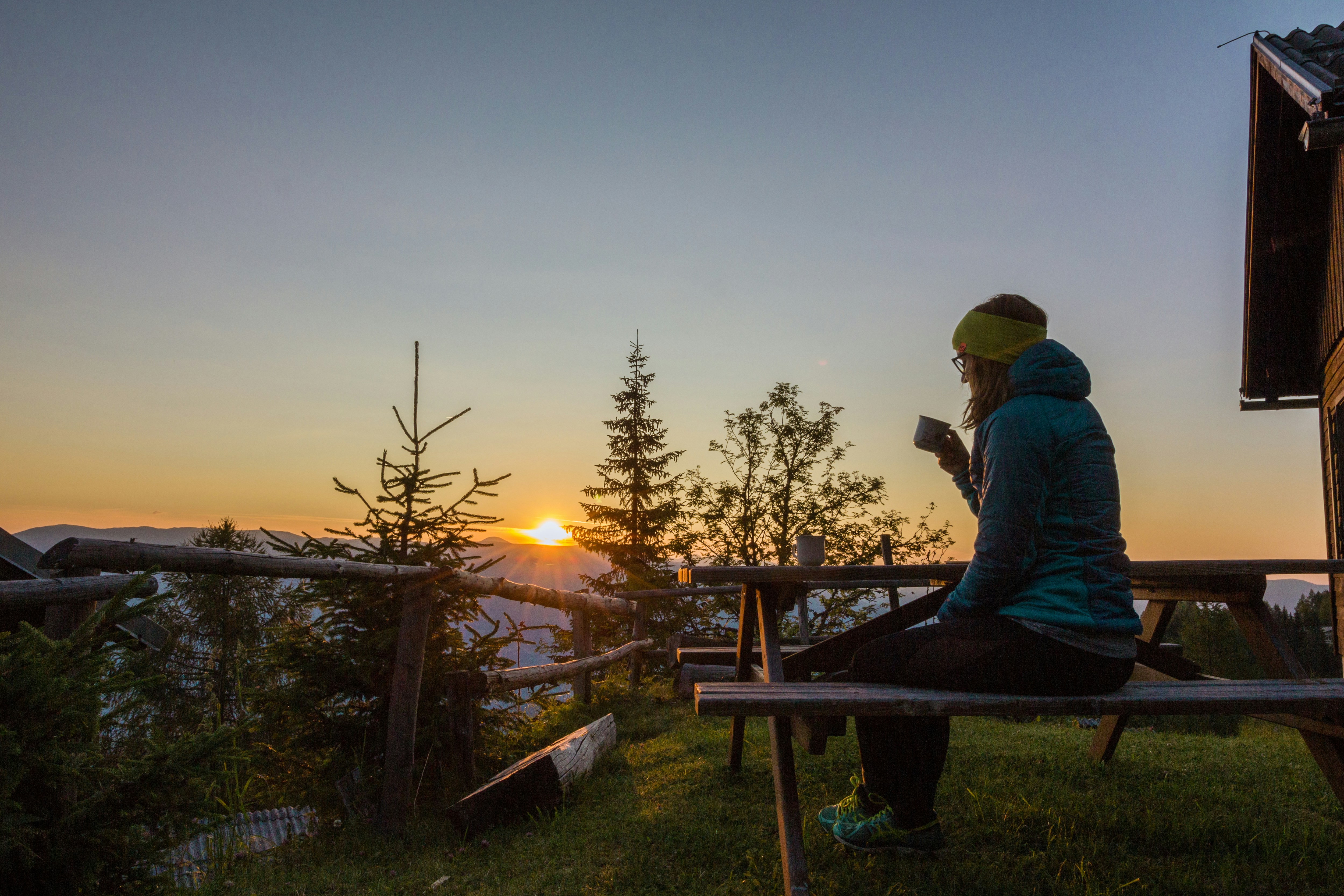 woman in blue bubble jacket sitting and having a coffee on mountain during sunrise
