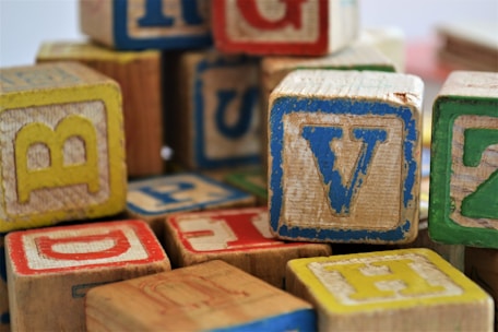 A pile of wooden alphabet blocks featuring various letters in different colors including red, blue, yellow, and green. The blocks appear well-worn, suggesting they have been frequently used or are vintage.