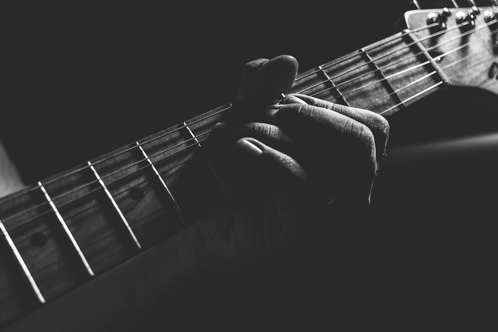Graustufenfoto einer Person, die Gitarrenhals und Saiten hält