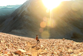 A sunlit morning scene with a person joyfully hiking on a mountain trail.