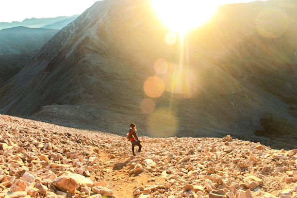 A sunlit morning scene with a person joyfully hiking on a mountain trail.