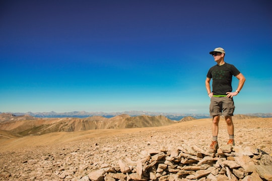 A vibrant traveler standing on a mountain peak at sunrise, wearing bold, stylish attire.