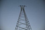 A tall metal transmission tower rises against a clear sky, with power lines extending outward from the structure.