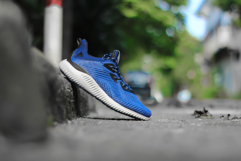 selective focus photography of unpaired blue and white adidas running shoe leaning on concrete pavement at daytime
