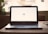 A laptop displaying the word 'Hi' on its screen is placed on a wooden table with a soft background blur. To the right, a pair of earphones is partially visible.