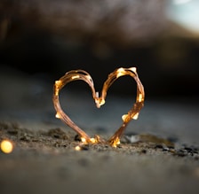 close-up photography of heart shaped fairy lite on brown sand